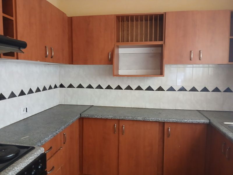 A functional kitchen featuring wood-look laminate cabinetry, granite-style countertops, and a decorative tiled backsplash with integrated stove and extractor fan.