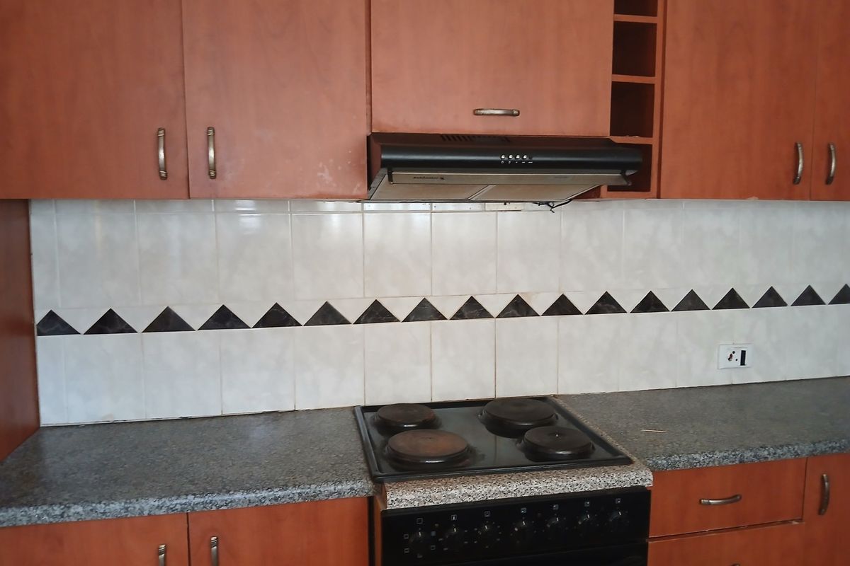A functional kitchen featuring wood-look laminate cabinetry, a granite-style countertop, and integrated cooking appliances with a decorative tiled backsplash.