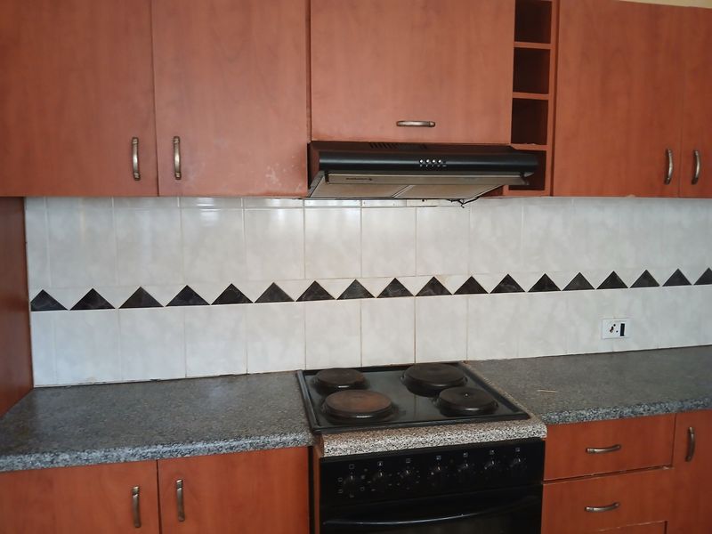 A functional kitchen featuring wood-look laminate cabinetry, a granite-style countertop, and integrated cooking appliances with a decorative tiled backsplash.