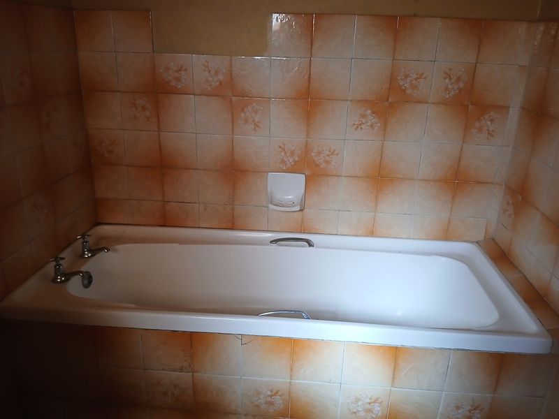 A dated bathroom featuring a built-in bathtub with chrome fixtures and patterned ceramic wall tiles.