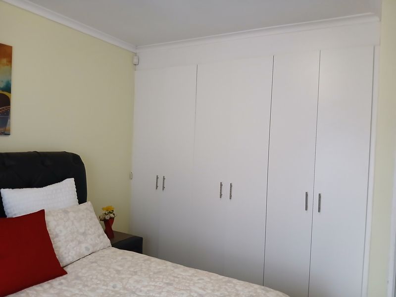 A bedroom featuring white built-in cupboards with modern handles and decorative cove cornicing.