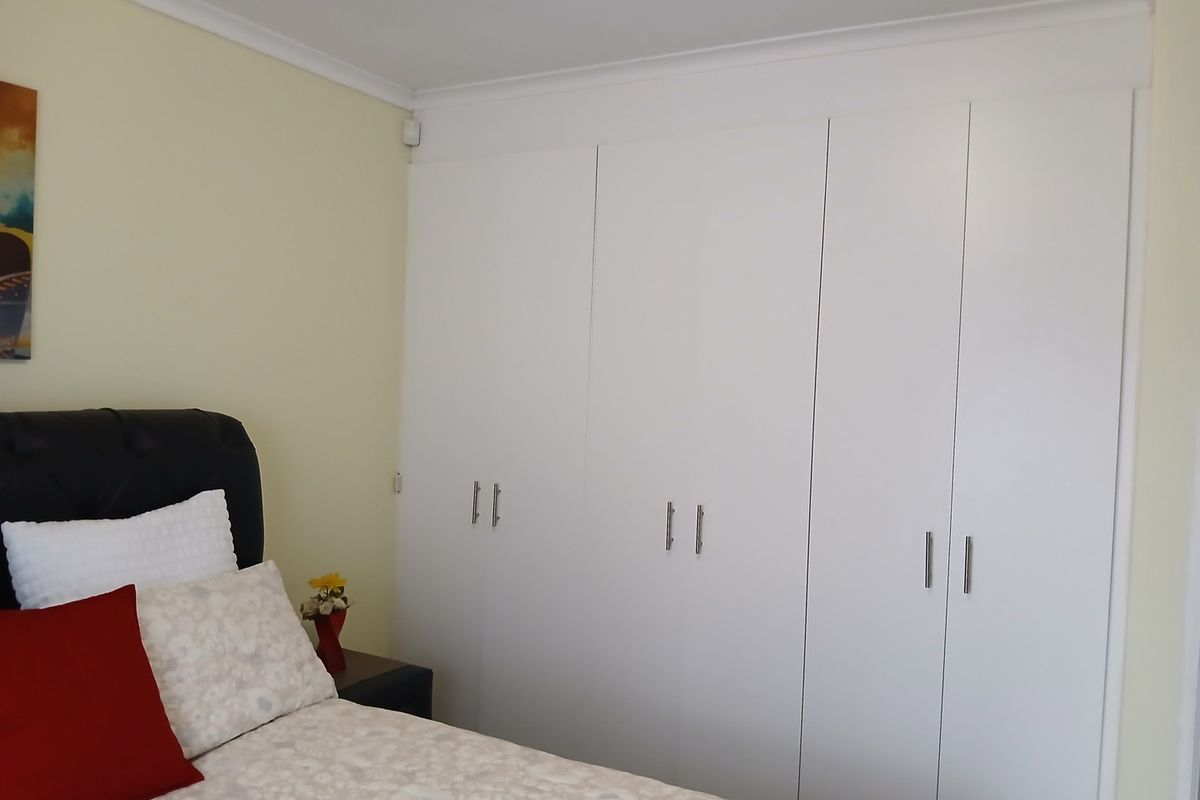 A bedroom featuring white built-in cupboards with modern handles and decorative cove cornicing.