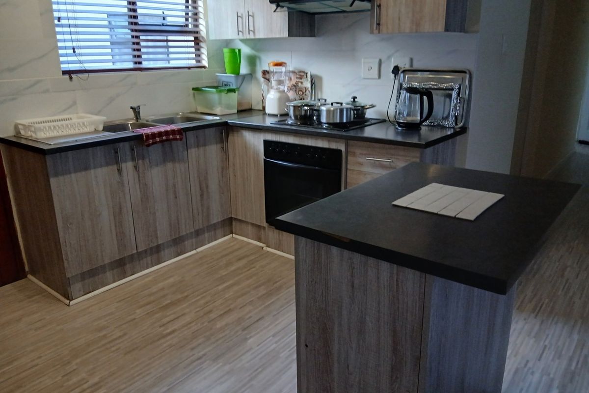 A functional kitchen featuring wood-look laminate cabinetry, dark countertops, a built-in oven with hob, and an extractor fan.