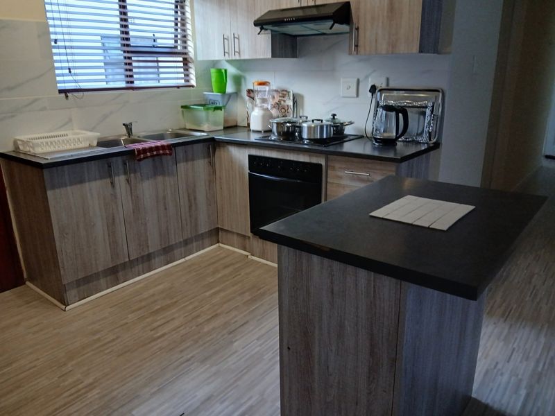 A functional kitchen featuring wood-look laminate cabinetry, dark countertops, a built-in oven with hob, and an extractor fan.
