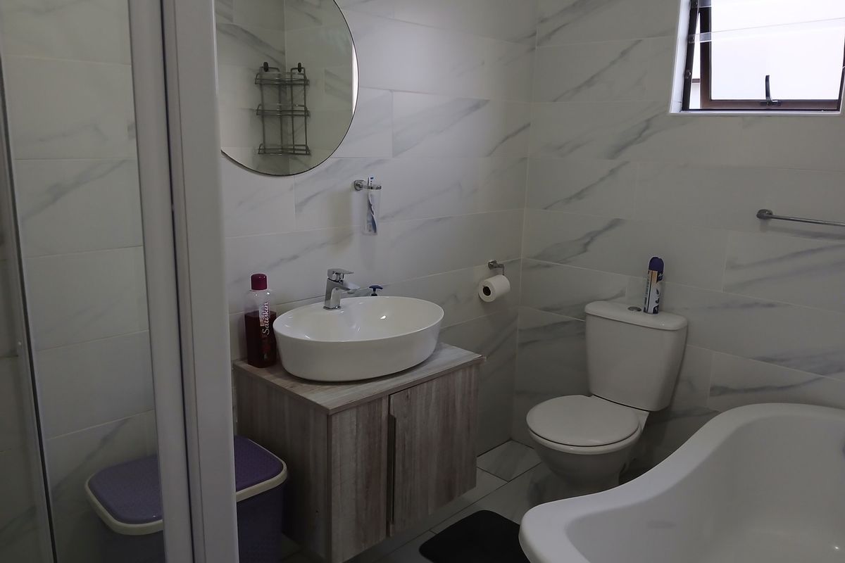 Modern bathroom featuring marble-look wall tiles, a vessel sink with vanity cabinet, a bathtub, and a separate shower enclosure.