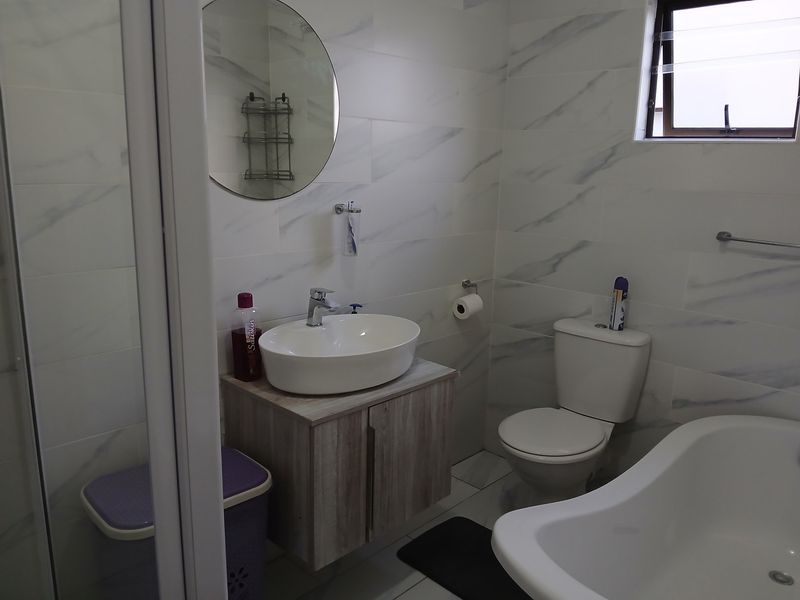 Modern bathroom featuring marble-look wall tiles, a vessel sink with vanity cabinet, a bathtub, and a separate shower enclosure.