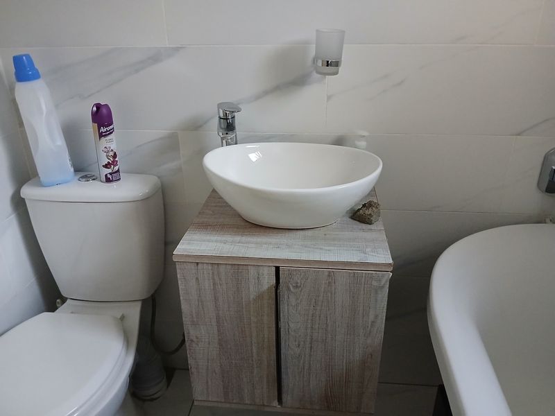 A modern bathroom featuring a vessel sink on a wood-finish vanity, a white toilet, and a bathtub with marble-look wall tiling.