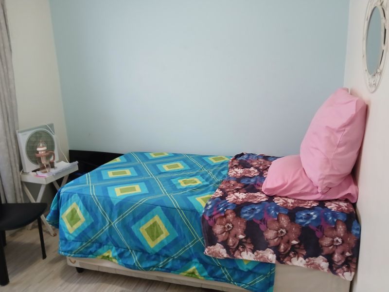 A simple bedroom featuring light-colored laminate flooring and a single bed, providing a functional and compact sleeping space.