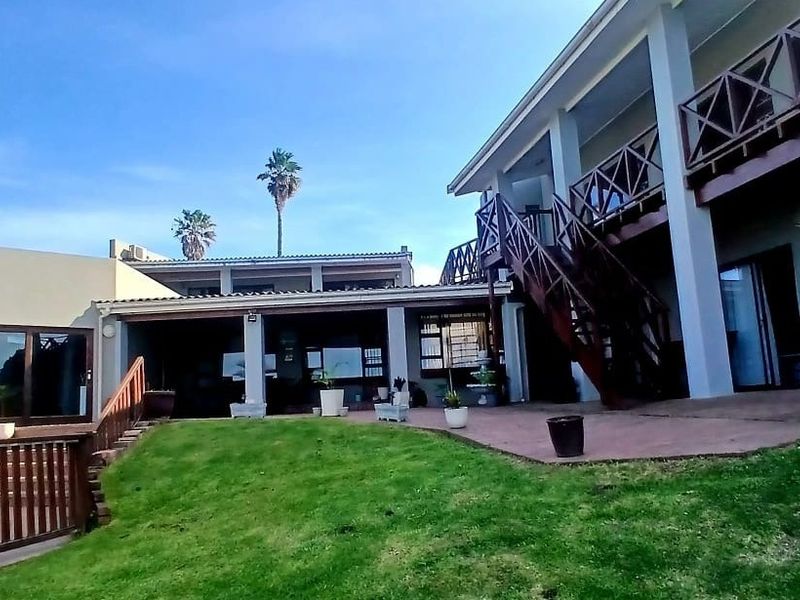 Rear view of the property featuring a paved patio, lawn, and a wooden staircase leading to an upper balcony.
