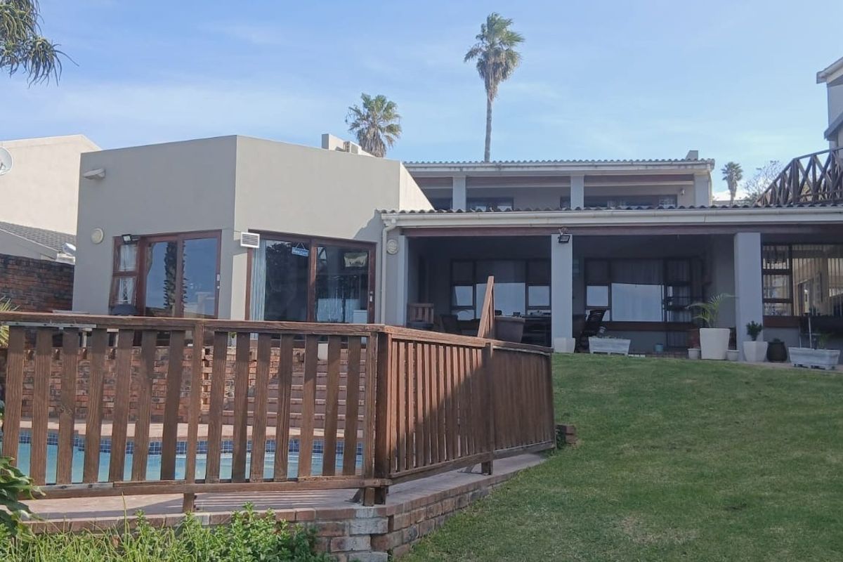 Rear view of the property featuring a swimming pool with a wooden deck, a covered patio area, and a lawn.