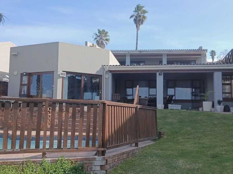 Rear view of the property featuring a swimming pool with a wooden deck, a covered patio area, and a lawn.