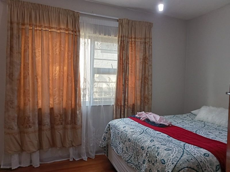 A bedroom featuring wooden flooring and a window fitted with security bars, providing natural light.