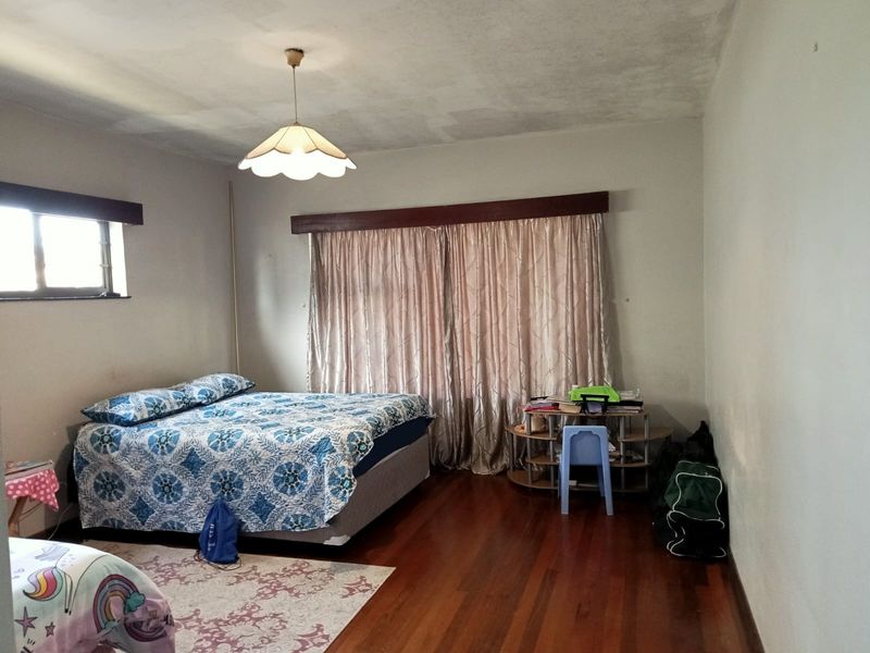 A spacious bedroom featuring polished hardwood flooring, a central pendant light fixture, and a timber curtain pelmet above the window area.