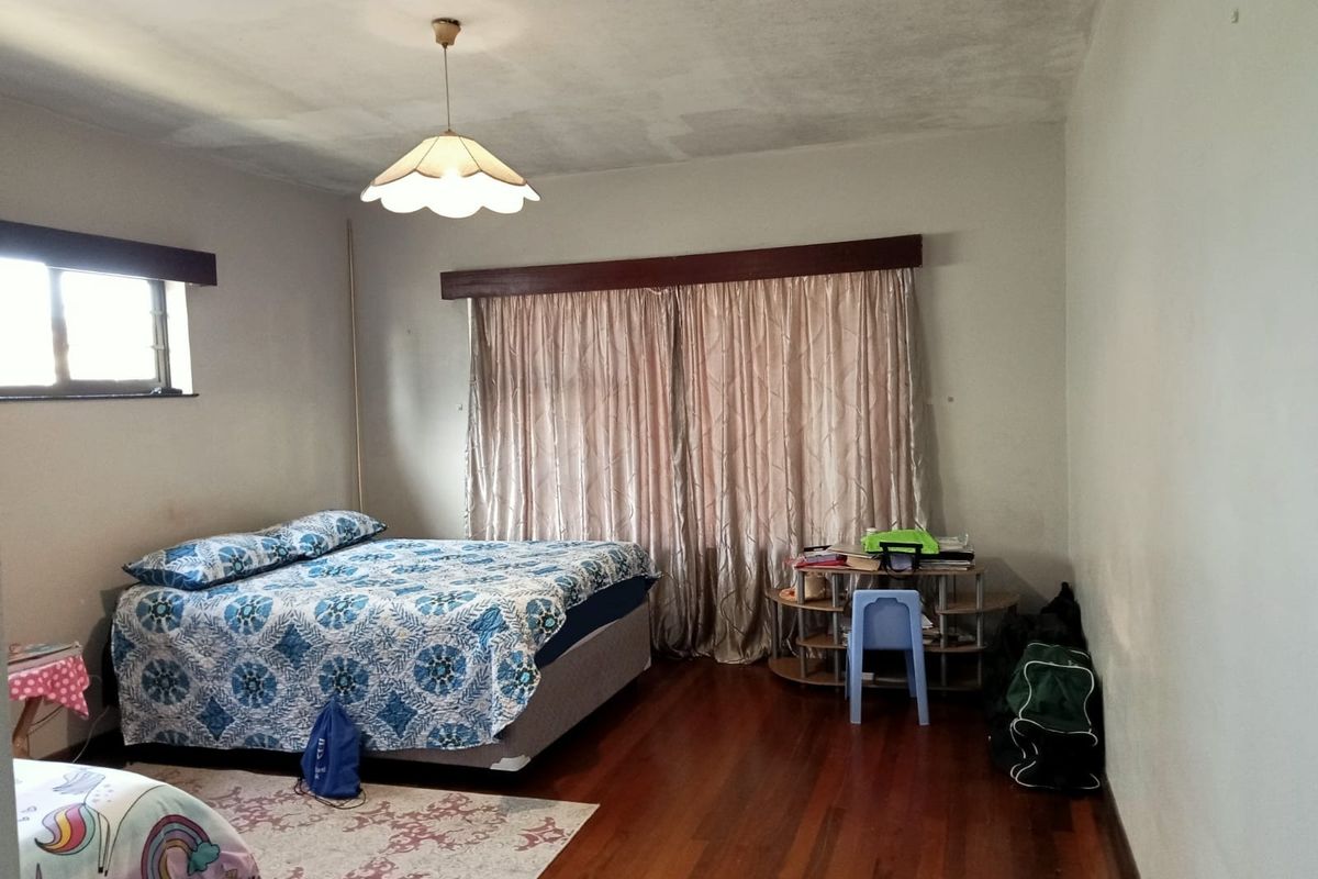 A spacious bedroom featuring polished hardwood flooring, a central pendant light fixture, and a timber curtain pelmet above the window area.
