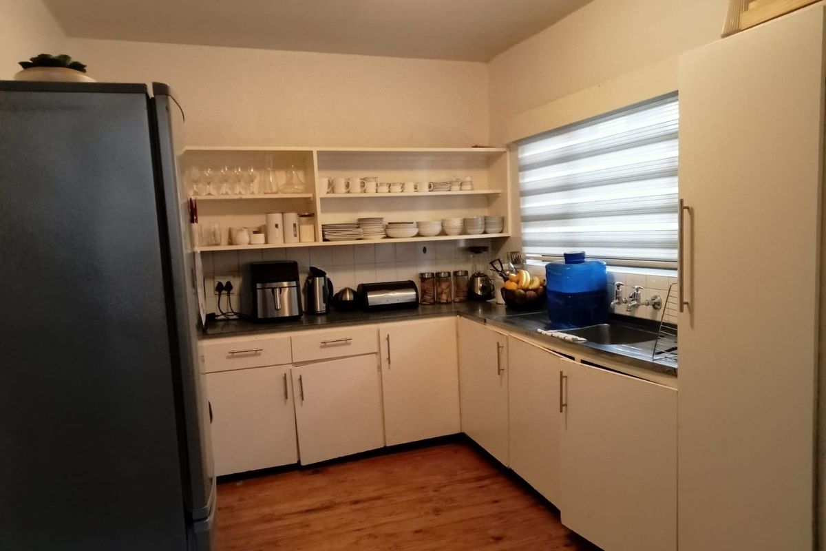 Functional kitchen featuring white cabinetry, open shelving, stainless steel sink, and timber-look flooring with a window providing natural light.
