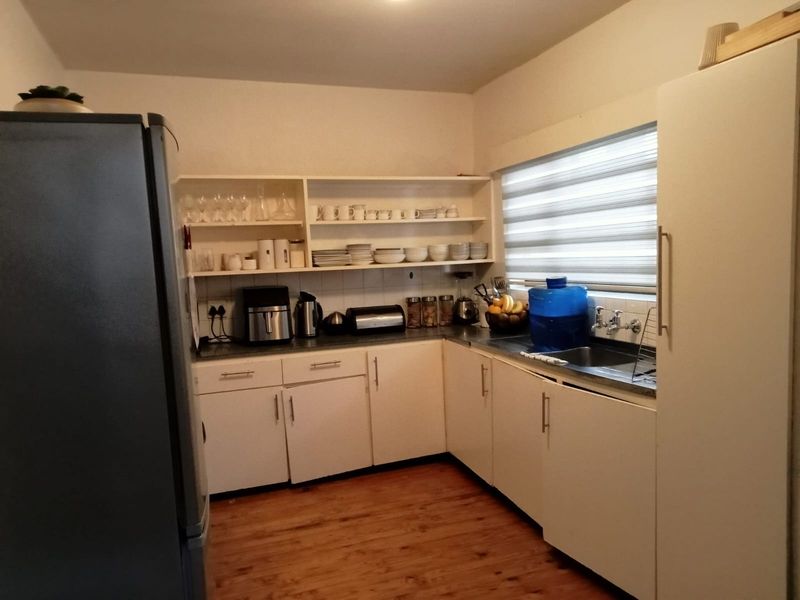 Functional kitchen featuring white cabinetry, open shelving, stainless steel sink, and timber-look flooring with a window providing natural light.