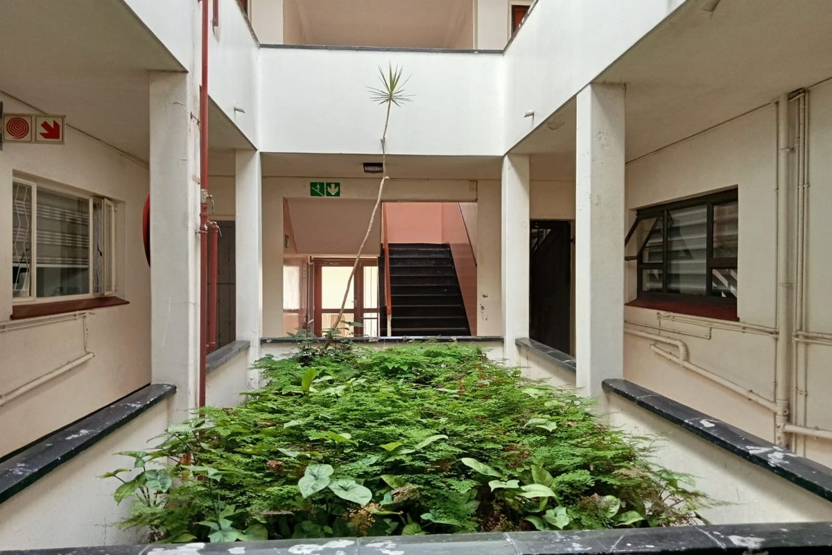 An open-air central atrium courtyard within an apartment complex, featuring a central garden bed, concrete pillars, and access staircases.