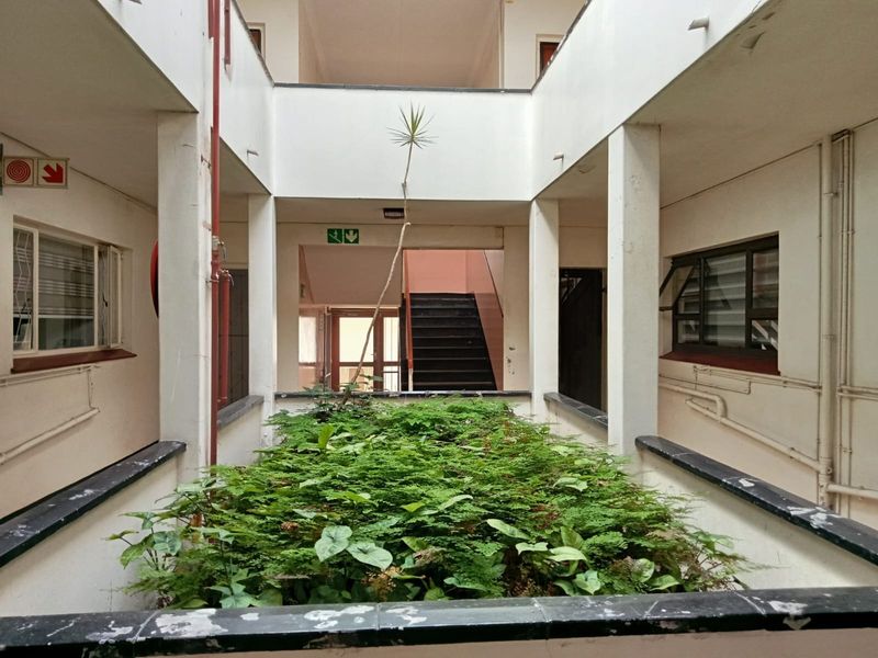 An open-air central atrium courtyard within an apartment complex, featuring a central garden bed, concrete pillars, and access staircases.