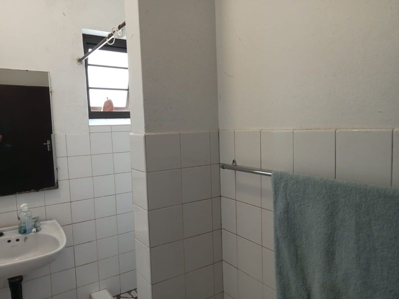 A functional bathroom featuring white wall tiles, a pedestal basin, and a window, currently in need of cosmetic updates.