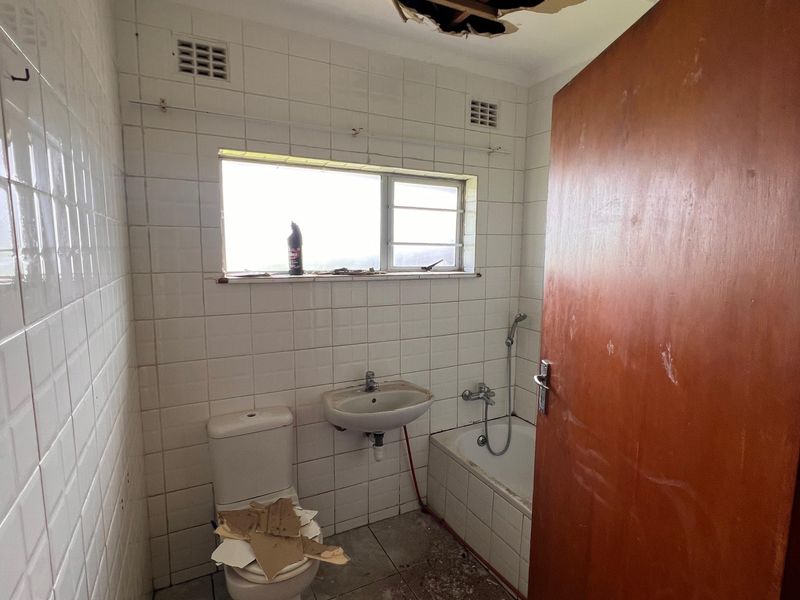 A bathroom in need of significant renovation, featuring a damaged ceiling, dated wall and floor tiles, and standard sanitary fixtures.