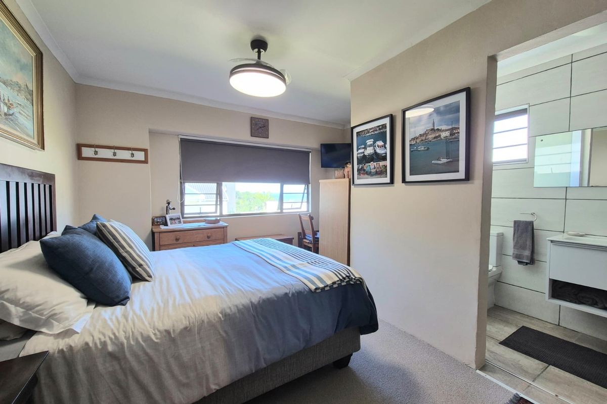 A well-maintained bedroom featuring a ceiling fan, roller blinds, and an adjoining en-suite bathroom with modern tiling and vanity.