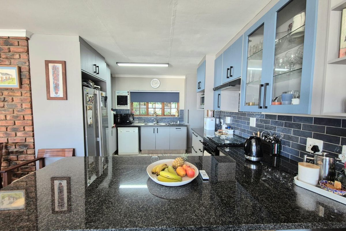 A well-appointed kitchen featuring granite countertops, a stylish subway tile backsplash, and a mix of blue and grey cabinetry with an exposed brick accent wall.