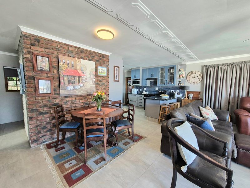 Open-plan living and dining area featuring an exposed brick wall, decorative ceiling molding, and a modern kitchen with island and built-in cabinetry.