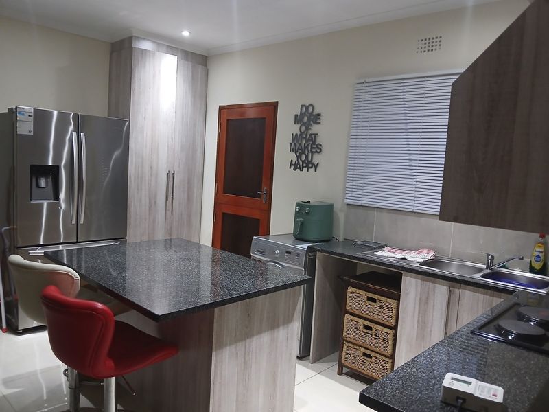 Modern kitchen featuring granite countertops, ample built-in cabinetry, a stainless steel double sink, and an electric hob with a functional island layout.