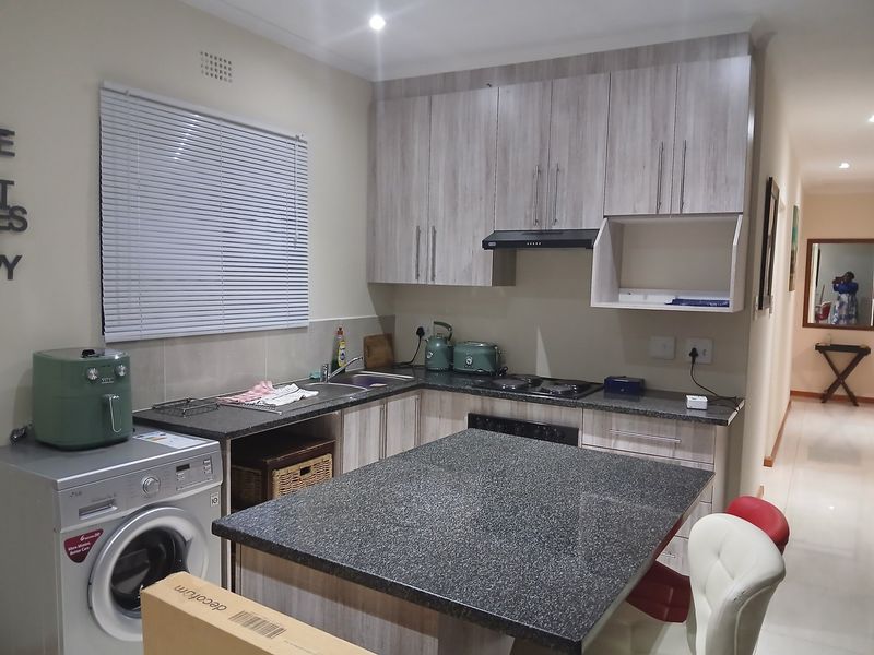 Modern kitchen featuring light wood-grain cabinetry, granite countertops, a central island, and integrated appliances, offering a functional and contemporary cooking space.
