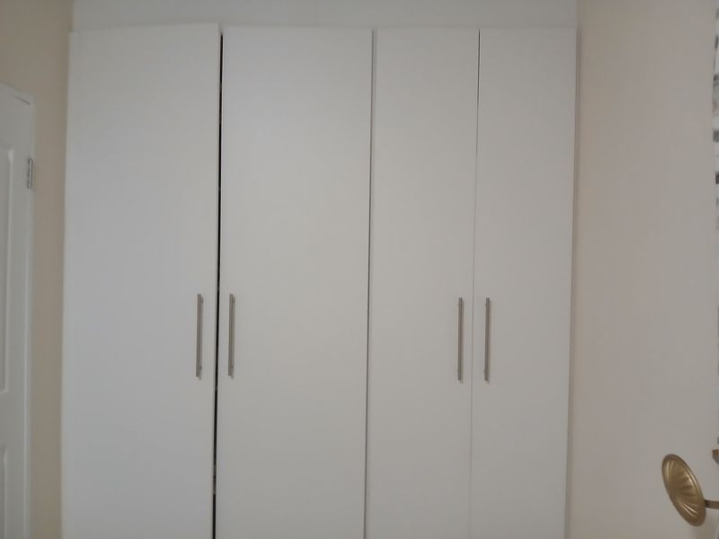A bedroom featuring clean, white built-in cupboards with modern silver handles, providing ample storage space.