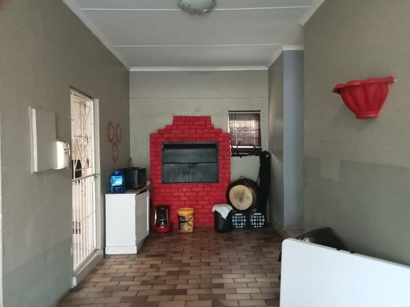 A covered patio area featuring a built-in brick braai, tiled flooring, and direct access to the home through a security gate.