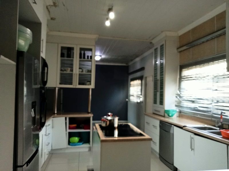 Kitchen featuring a central island with cooktop, built-in cabinetry, and double sink, showing signs of ceiling water damage requiring repair.