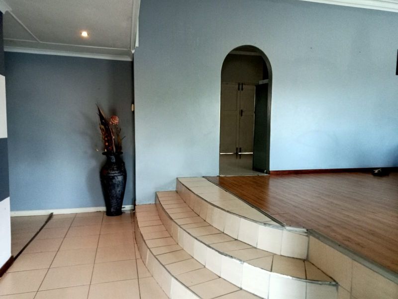 An interior living space featuring a raised platform with laminate flooring, tiled lower level, and an arched doorway leading to an adjacent room.