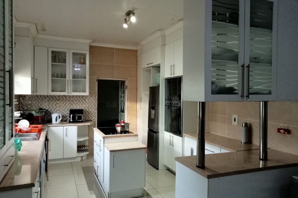 A functional kitchen featuring white cabinetry, stone countertops, a central island with a hob, built-in oven, and tiled backsplash.