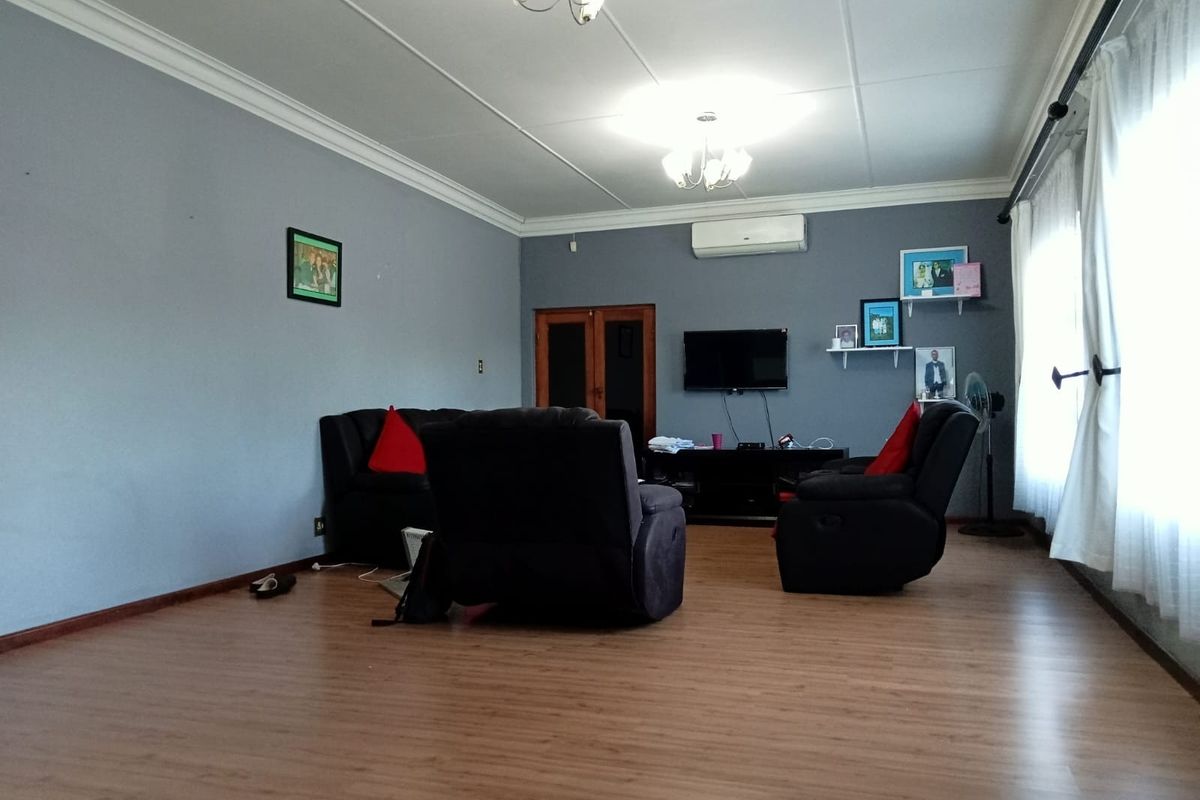 A spacious living room featuring laminate flooring, crown molding, and a wall-mounted air conditioning unit.