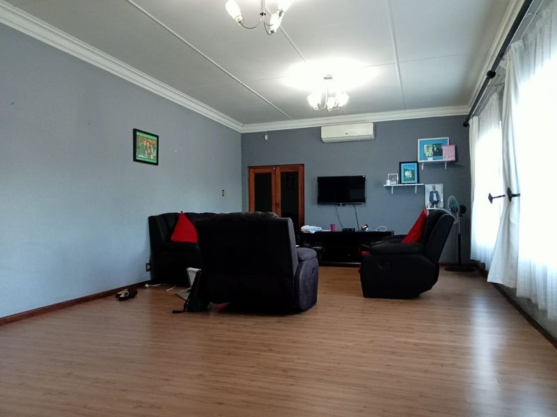 A spacious living room featuring laminate flooring, crown molding, and a wall-mounted air conditioning unit.
