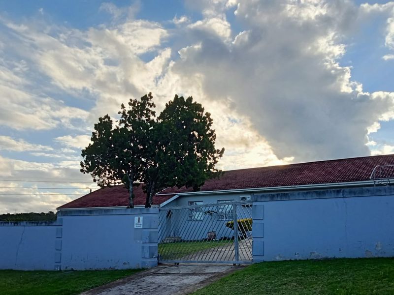 Front view of a residential property featuring a tiled roof, paved driveway, and a secure metal gate set within a perimeter wall.