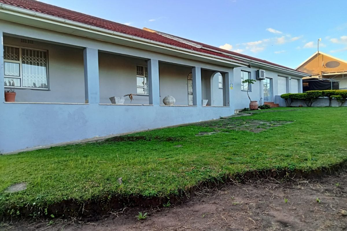 A rear view of the house featuring a covered patio, tiled roof, and a spacious lawn area.