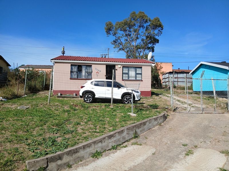 Front view of a single-story house featuring a corrugated metal roof, security bars on windows, and a concrete retaining wall with perimeter fencing.