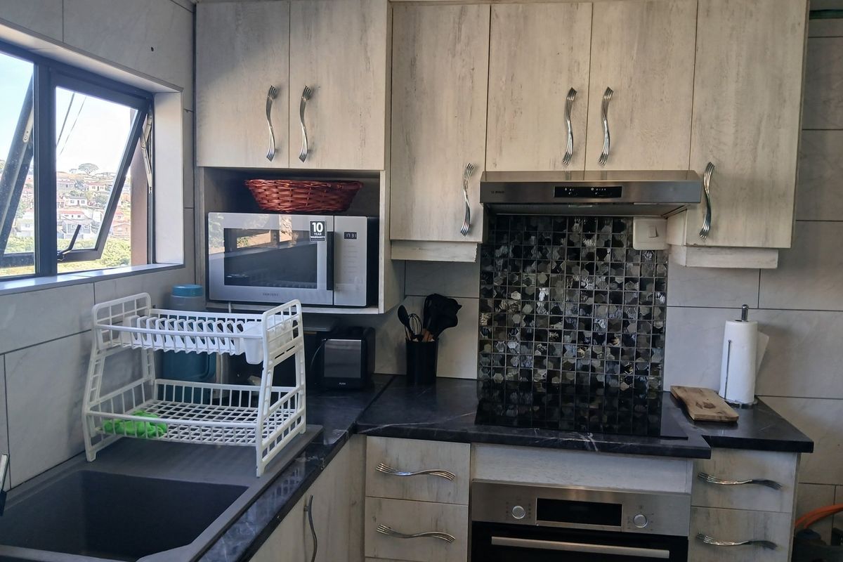 A functional kitchen featuring light wood-grain cabinetry, dark stone-look countertops, a mosaic tile backsplash, and integrated stainless steel appliances.