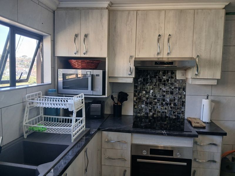 A functional kitchen featuring light wood-grain cabinetry, dark stone-look countertops, a mosaic tile backsplash, and integrated stainless steel appliances.