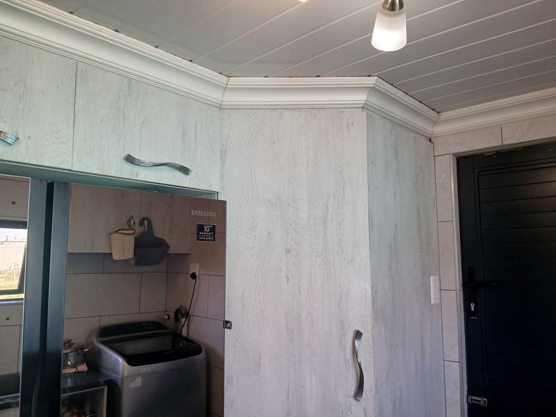 A functional laundry area featuring built-in cabinetry, tiled wall finishes, and a panelled ceiling with decorative cornice detailing.