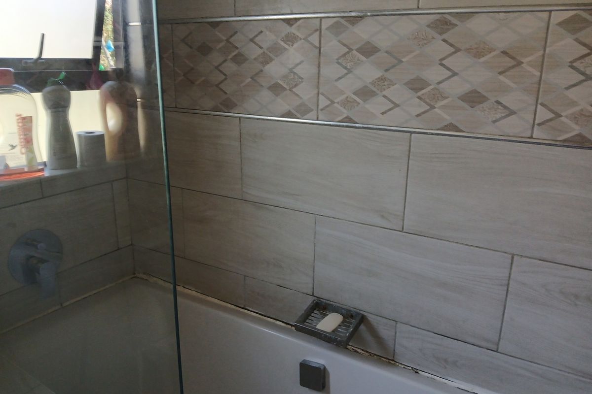 A bathroom featuring a built-in bathtub with a glass shower screen and decorative wall tiling.