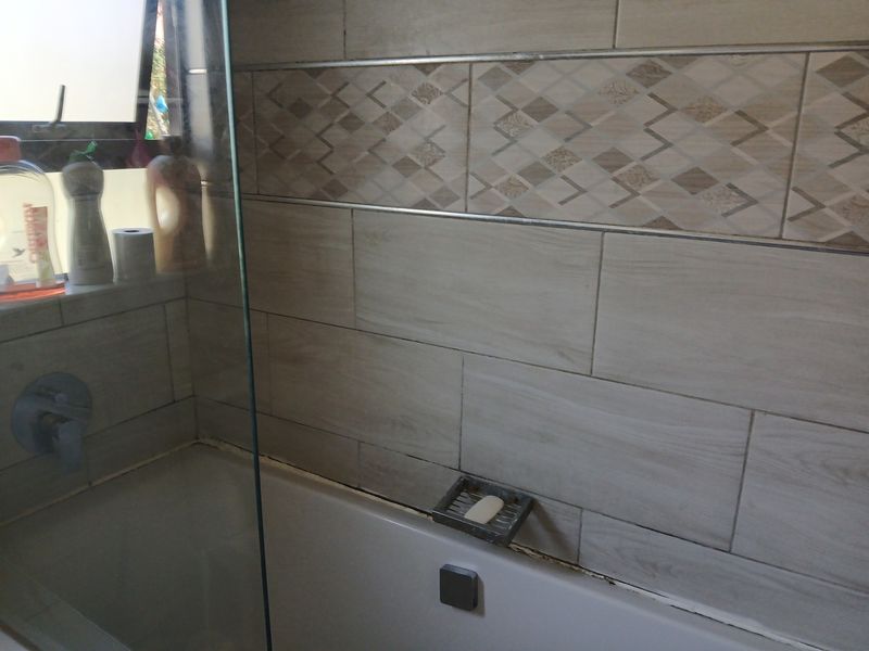 A bathroom featuring a built-in bathtub with a glass shower screen and decorative wall tiling.