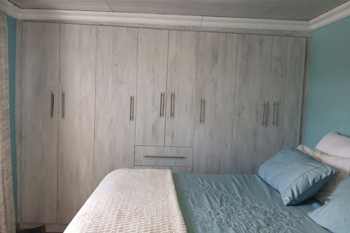 A bedroom featuring extensive floor-to-ceiling built-in cupboards with a light wood-grain finish and modern metal handles.