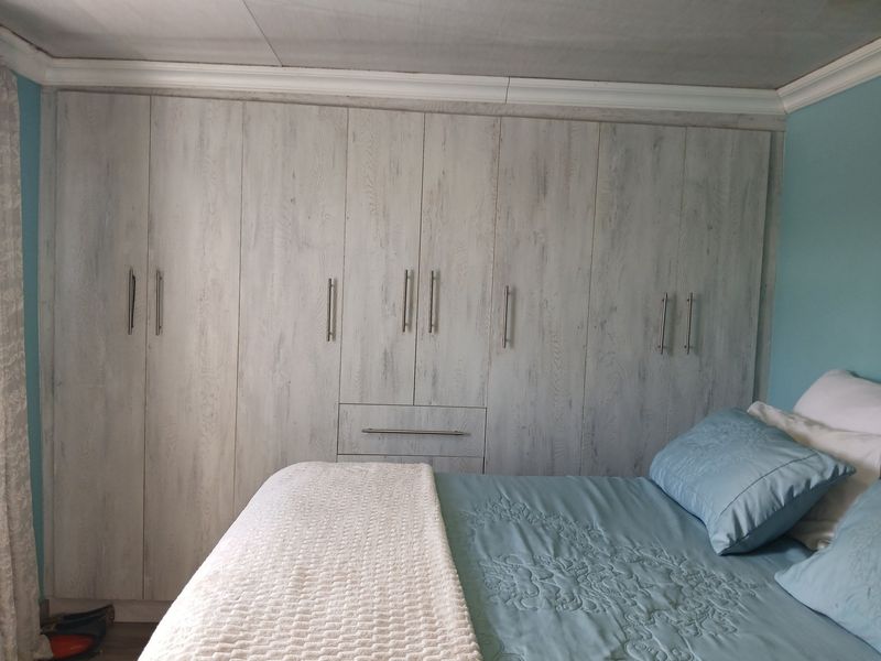 A bedroom featuring extensive floor-to-ceiling built-in cupboards with a light wood-grain finish and modern metal handles.