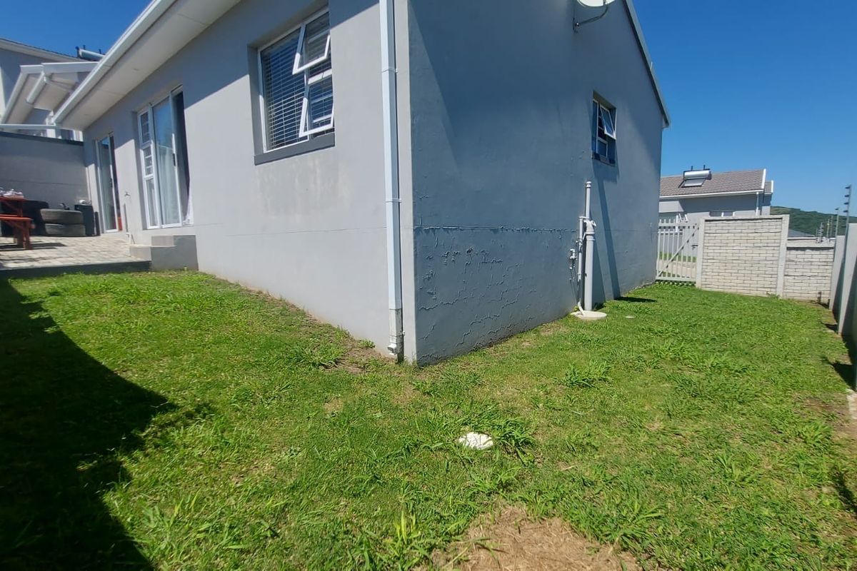 Rear exterior view of the townhouse featuring a small lawn, paved patio area, and visible cracking on the exterior wall plaster.