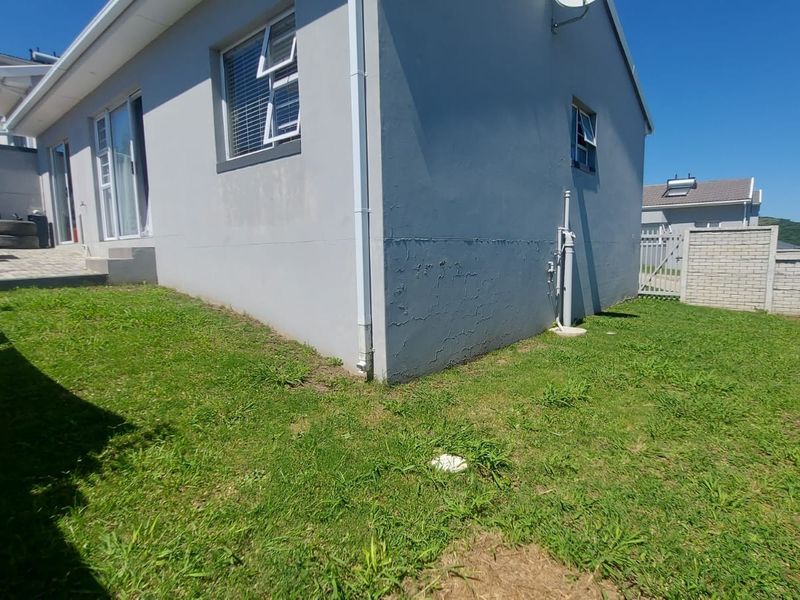 Rear exterior view of the townhouse featuring a small lawn, paved patio area, and visible cracking on the exterior wall plaster.