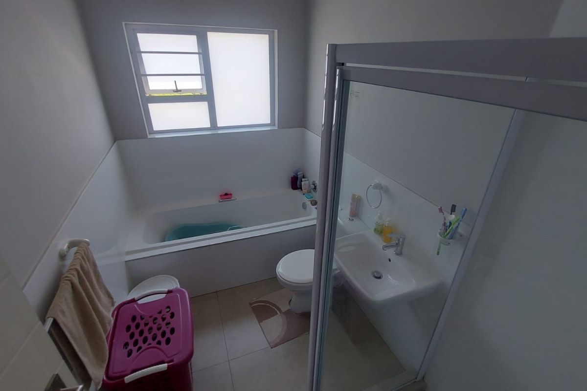 A functional bathroom featuring a built-in bathtub, separate shower enclosure, pedestal washbasin, and toilet with neutral tiled finishes.