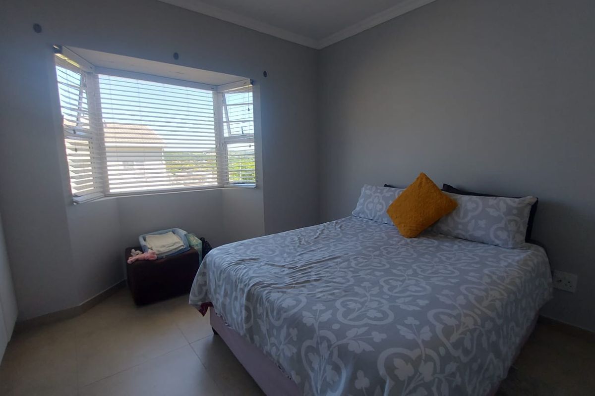 A well-lit bedroom featuring tiled flooring, built-in cupboards, and a bay window that provides natural light and exterior views.